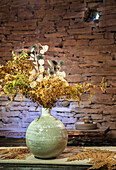 Dried flower arrangement in ceramic vase in front of rustic brick wall