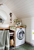 Waschmaschine und Waschtisch in Badezimmer mit Holzverkleidung und Pflanzendeko