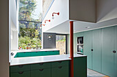 Custom kitchen with green cabinet fronts in a high ceiling room with garden view