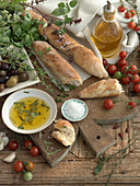 Stilleben mit Baguette, Olivenöl, Basilikum, Oregano, Tomaten, Salz und Oliven
