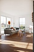 Gray upholstered sofa with cushions and wooden stool in bright living room, star decoration on patio door