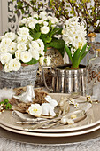 Easter table setting with silverware and rabbit figurines, white primroses and hyacinths on a table