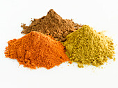 Three heaps of spices on a light background (curry, chilli powder, clove powder)