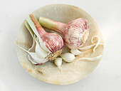 Two garlic bulbs in a small bowl on a light background