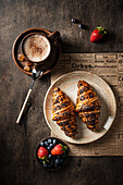 Croissants on a plate with a cup of coffee and fresh berries on a wooden table