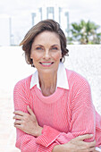 Frau in pinkfarbenem Pullover und weißem Hemd am Strand