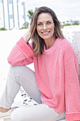 Frau in pinkfarbenem Pullover und weißer Hose