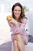 Long-haired woman with an orange in a short crochet dress