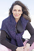 Long-haired woman in a dark coat with a sweater over her shoulders on the beach