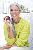 Grauhaarige Frau mit einem Apfel in grüngelbem Strickpullover