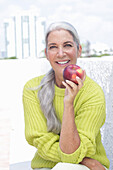 Gray-haired woman with an apple in a green and yellow knit sweater