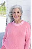 A grey-haired woman wearing a pink jumper on the beach