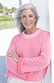 Grauhaarige Frau in pinkfarbenem Pullover am Strand