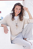 Happy, long-haired woman in light, casual knitted jumper and trousers