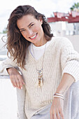 A happy, long-haired woman wearing a light-coloured, casual knitted jumper