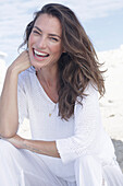 Happy, long-haired woman in white jumper and white trousers on the beach