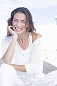 Happy, long-haired woman in white jumper and white trousers on the beach