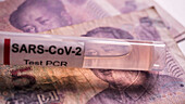 Coronavirus test vial on Chinese banknotes, conceptual image