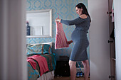 Pregnant woman getting dressed in bedroom