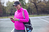 Pregnant woman using smart phone on tennis court