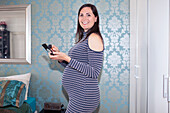 Smiling pregnant woman putting on makeup in bedroom