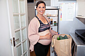 Smiling pregnant woman in sports bra unloading groceries