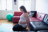 Pregnant woman touching baby bump on living room floor