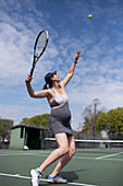 Pregnant woman serving tennis ball on sunny tennis court