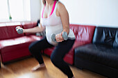 Pregnant woman working out with dumbbells at home