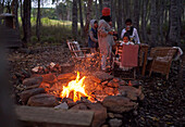 Family relaxing at table by campfire in woods