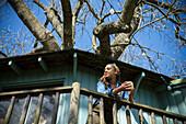 Smiling young woman drinking coffee on tree house balcony