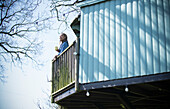 Young woman with coffee on sunny tree house balcony