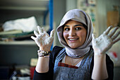 Happy female artist in hijab with clay covered hands