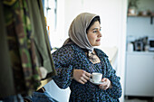 Thoughtful Muslim woman in hijab drinking coffee