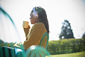Woman with headphones and yoga mat drinking coffee outside