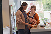 Happy women friends cutting cake in kitchen