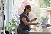 Pregnant woman with credit card online shopping at laptop