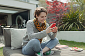 Smiling woman using smart phone on patio lounge chair