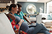 Pregnant couple using laptop on living room sofa