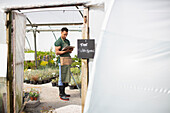 Male garden shop owner with clipboard in greenhouse