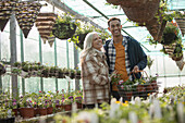 Happy couple shopping for hanging baskets in greenhouse