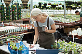 Female garden shop owner with coffee working in greenhouse