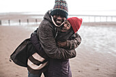 Happy playful couple hugging on wet winter beach