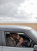 Happy couple drinking coffee in car on winter beach
