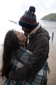Affectionate couple wrapped in a blanket on winter beach