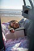 Woman reading book in back of car on beach