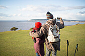 Hiker couple with camera phone on cliff with ocean view