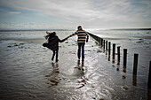 Couple holding hands running on sunny wet winter beach