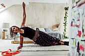Woman exercising in side plank on bedroom rug