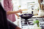 Woman cooking in wok on kitchen stove